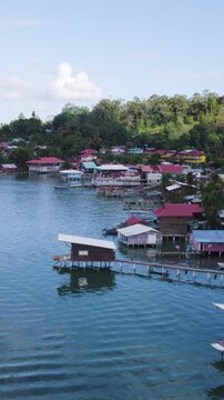 Vertical aerial view of rustic homes along the coastline of Bastimentos Island, Panama, featuring stilt houses with lush greenery in the background.