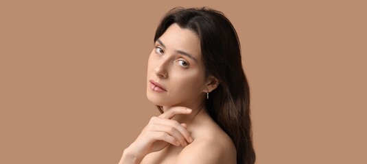 Young woman with nose, lip and ear piercing on beige background