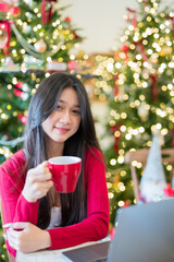 A young woman is enjoying a warm drink next to a Christmas tree in a festive holiday atmosphere.