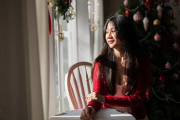 A young woman sat near the Christmas tree with a book, looking out the window.