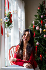 A young woman sat near the Christmas tree with a book, looking out the window.