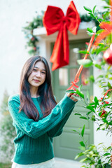 A young woman is decorating a Christmas tree with ornaments, getting ready for the winter holiday season. It's a celebratory scene in front of the house.