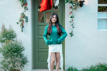A young woman is decorating a Christmas tree with ornaments, getting ready for the winter holiday season. It's a celebratory scene in front of the house.