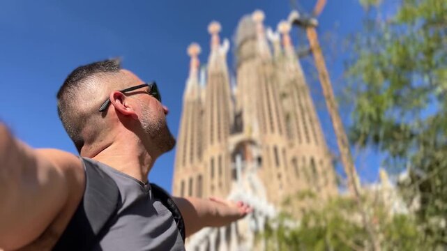 Latin american travel tourist male taking a selfie in front of the iconic Sagrada Familia cathedral on a sunny day, enjoying his summer vacation and exploring the architecture in Barcelona, Spain
