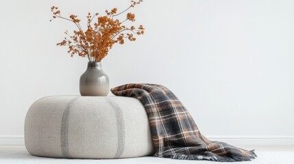 Gray vase, dried plants, plaid blanket on comfy pouf stool