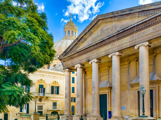 Obraz premium Valletta, Malta — view of St Pauls Pro-Cathedral and dome of the Basilica of Our Lady of Mount Carmel behind a classical portico, sunny town scene