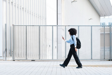 side view of Woman walking city, using smartphone on urban street