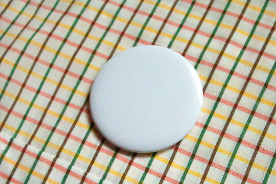 Mockup badge pinned to colorful plaid fabric. Empty button badge on clothes pocket close-up. Fashion mockup pin on vintage check fabric. Round badge mockup on textile background. Circle badge mockup