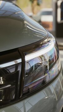Vertical shot of sleek LED headlight and modern car front with reflecting light on display in showroom