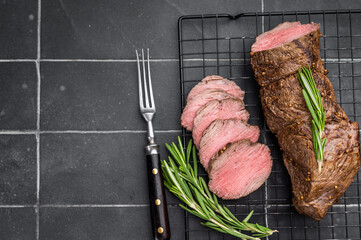 Sliced roast beef cooked medium rare with rosemary and pepper. Juicy roasted beef tenderloin on dark background with copy space.