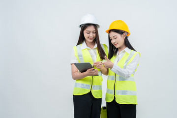 Two Asian women engineers in safety vests analyze construction data on a tablet, symbolizing smart industry solutions, teamwork collaboration, digital workflow, and modern professional safety culture.