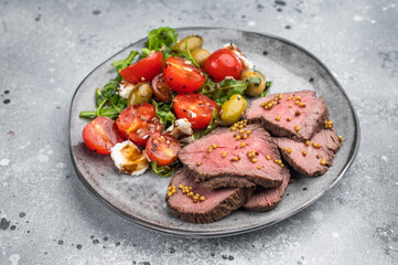Gourmet beef roast sliced medium rare with Mediterranean salad on ceramic plate light background overhead food photo