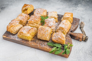 Greek custard pie bougatsa made with flaky filo pastry sliced into squares served on wooden board with powdered sugar