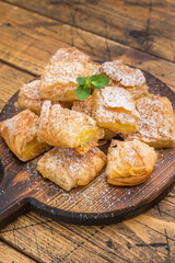 Greek custard pie bougatsa made with flaky filo pastry cut into squares served on round wooden board with powdered sugar