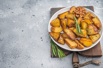 Crispy baked potato chunks with skin, rosemary and garlic. Homemade vegetarian food on wooden board