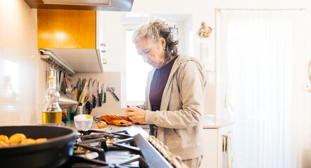 Senior woman is peeling vegetables while cooking in her bright kitchen