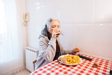 Senior woman enjoying a solitary meal with wine at a checkered table in her kitchen