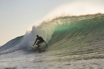 Surfer Tucked Inside Translucent Barrel at sunset