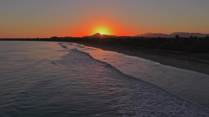 Sunrise over a tropical beach in Miches. The orange sun rises behind a mountain, reflecting on the ocean waves. Ideal for travel and nature concepts