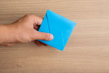 Top view of a hand holding a blue envelope on a wooden background with copy space. Perfect for communication concepts, email marketing, invitations, business messages, and announcement designs
