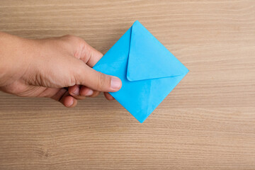 Top view of a hand holding a blue envelope on a wooden background with copy space. Perfect for communication concepts, email marketing, invitations, business messages, and announcement designs