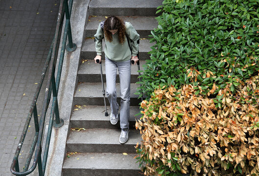 Chica con muletas tras cirug&iacute;a de operaci&oacute;n de rodilla en rehabilitaci&oacute;n bajando escalera paso a paso con cuidado