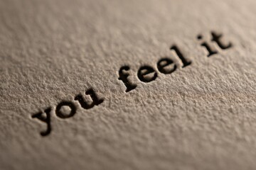 Top down extreme macro photograph of the sentence "you feel it" typed on thick cream paper, mechanical indentation from type bars, organic paper fibers, shallow focus, soft side lighting, 