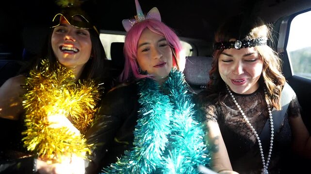 Three cheerful young women in festive costumes singing, dancing, and laughing together in the back seat of a car, heading to a new year's eve celebration or a fun costume party