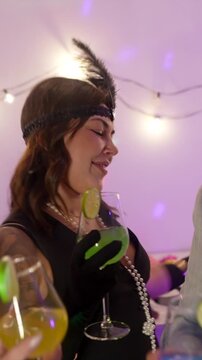 Three happy young women in festive costumes dancing, laughing, and toasting with colorful cocktails during a lively new year's eve party celebration at home under sparkling disco lights