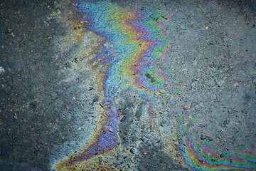 Oil slick creates a colorful iridescent pattern on wet asphalt, symbolizing pollution and abstract beauty