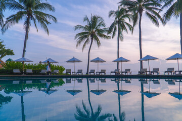 Beautiful sunrise sky with palm trees by seaside pool reflecting water, luxury tropical resort atmosphere