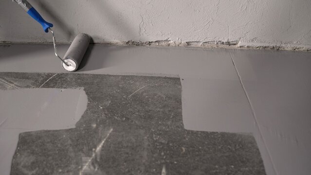 Close-up view of a skilled worker applying a gray epoxy resin coating to a concrete floor using a paint roller for renovation