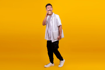 Young man walking with laptop and coffee in hand looking relaxed