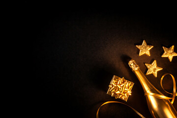 Golden champagne bottle with small gift box and shiny stars on black background for minimalist luxury new year celebration and festive holiday season layout design