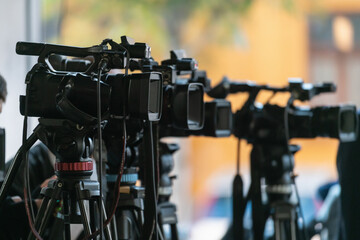 TV cameras lined in a row recording formal press conference. Highlights media coordination, structured setup, and clear communication environment.