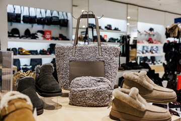 A fuzzy gray tote bag with matching pouch surrounded by warm, fur-lined winter shoes in a retail setting. Cozy, seasonal fashion theme with ample product variety