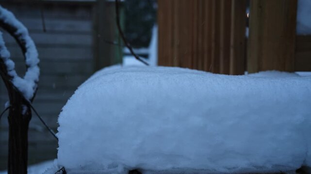 Fresh snow falling on a wooden deck railing in a quiet residential yard during the seasonal transition. Lateral movement.