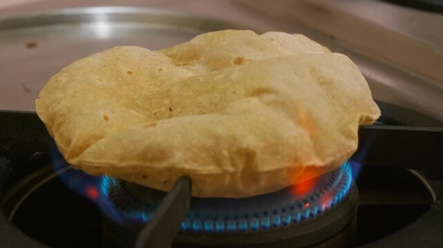 Close-up shot of a pulka (phulka) puffing up directly over a gas stove flame at home. internal shot, stable shot, 4k.