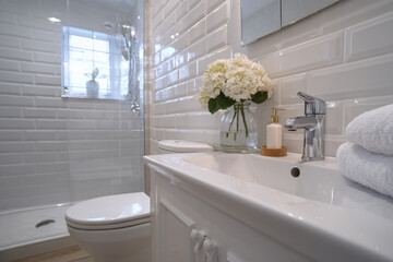 Modern bathroom with white subway tile walls, ceramic sink, chrome faucet, and fresh flowers