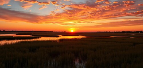Sun dips below horizon, painting a Virginia salt marsh in warm hues Tidal waters reflect fiery sky,  coastal wetland,  evening