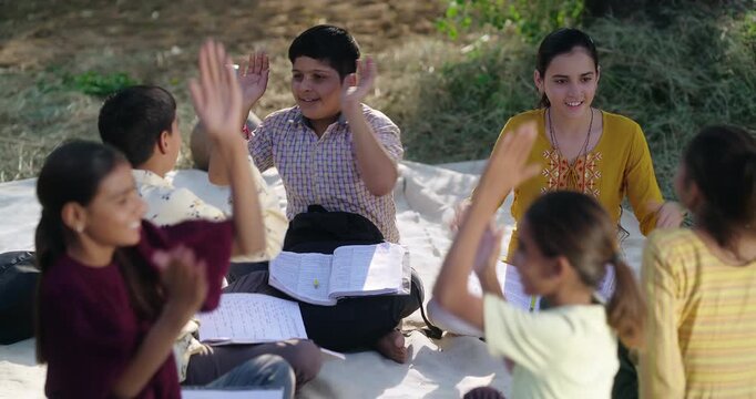 Indian villager teen boy girl sitting on mat enjoy desi life have fun joy outdoor rural area. Happy young child group play hand clap funny game spend break time open air field day time ground place