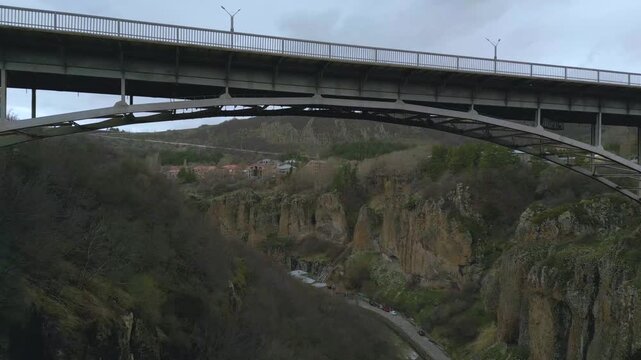Aerial drone video capturing a long modern bridge spanning a deep rocky canyon in jermuk armenia with dramatic cliffs forested slopes, cloudy sky creating cinematic travel and infrastructure landscape