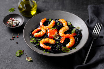 Black spaghetti pasta with shrimps and red caviar, garnished with fresh greens. Dark grey background. Close up.