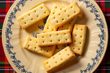 Classic Scottish shortbread fingers on ornate plate, tartan backdrop, traditional tea time treat. Close up.