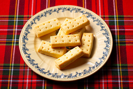 Classic Scottish shortbread fingers on ornate plate, tartan backdrop, traditional tea time treat. Close up.