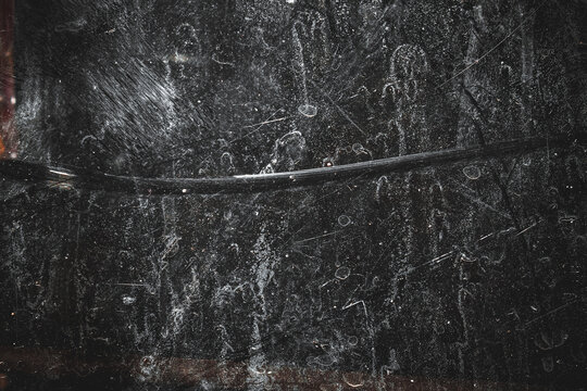 Abstract black grunge textured background with white scratches, stains, and dust effects. The rough, worn surface creates a dramatic, dark, and artistic impression.