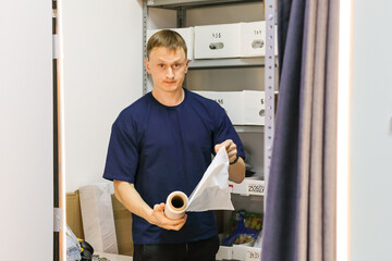 Man in blue shirt presenting roll of plastic wrap beside storage shelves. Worker displaying...