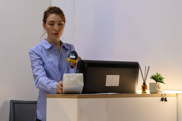 Woman scanning package on counter at pickup point. Staff uses barcode reader on wrapped item placed...