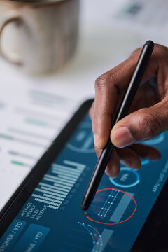 Black man using digital pen interacting with tablet displaying financial charts and analytics, hand holding stylus making notes on touchscreen, closeup of technology in business setting
