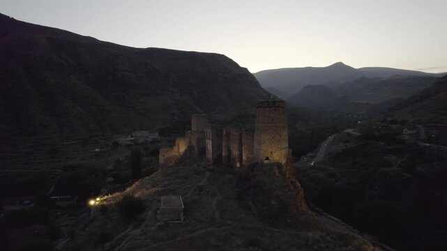 An ancient Khertvisi Fortress illuminated at dusk, standing on a high hill in the Samtskhe Javakheti region of Georgia and overlooking a dramatic mountainous landscape